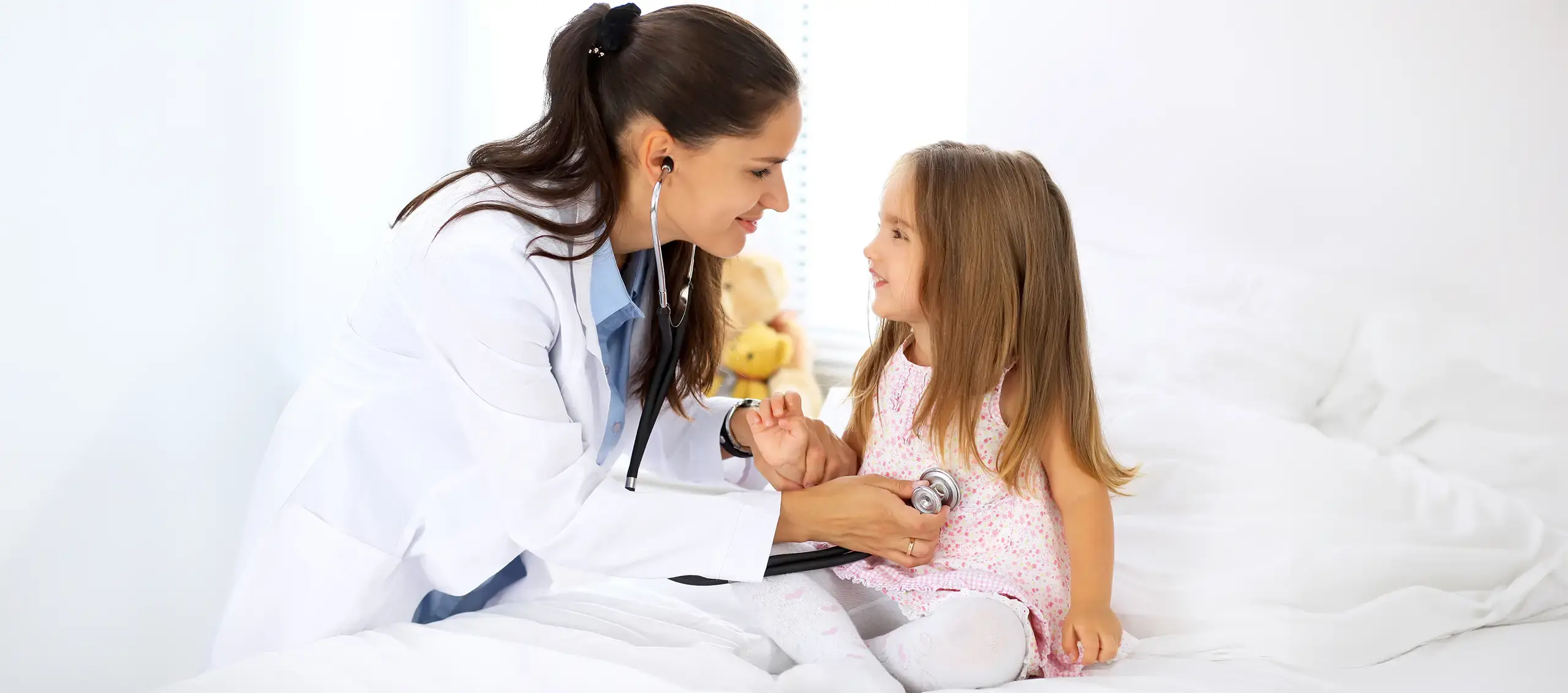 Woman doctor in lab coat using stethoscope on young girl